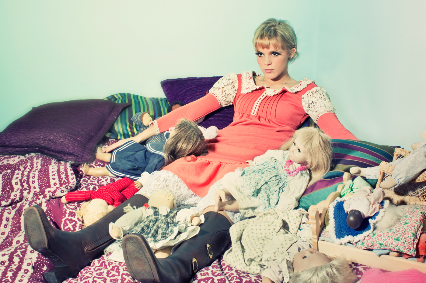 Photo of young blonde woman as a doll sitting on bed. Conceptual work by Oakland photographers Ella Sophie