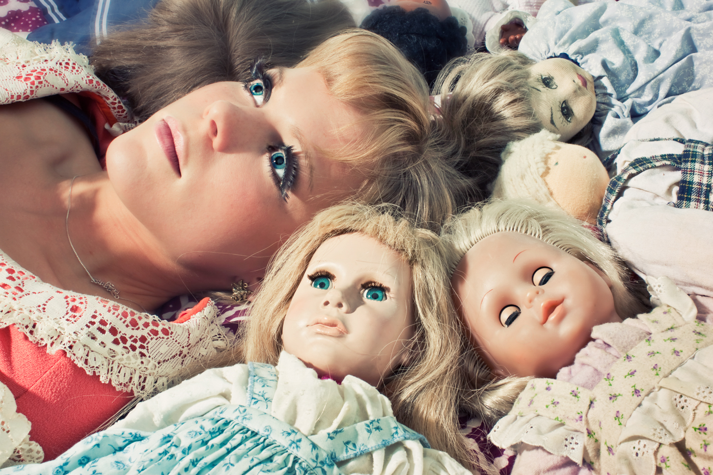 Blond woman with blank stare surrounded by dolls. Feminist photographers Ella Sophie. San Francisco CA