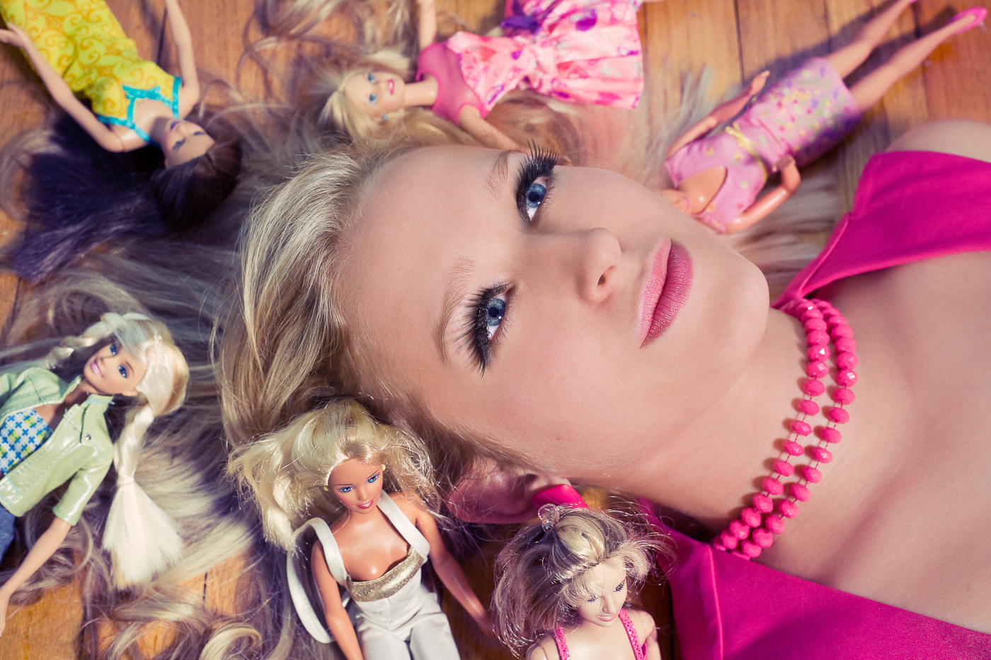 Young woman poses as doll surrounded by barbies. Art about Objectification of women in the Doll Collection