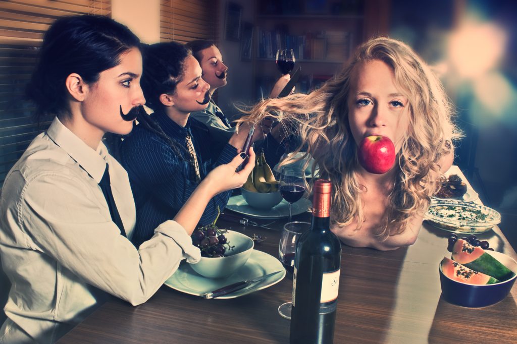Personal work by Ella Sophie. Edible, she is consumable. A woman with an apple in her mouth is feasted on at a dinner table. 