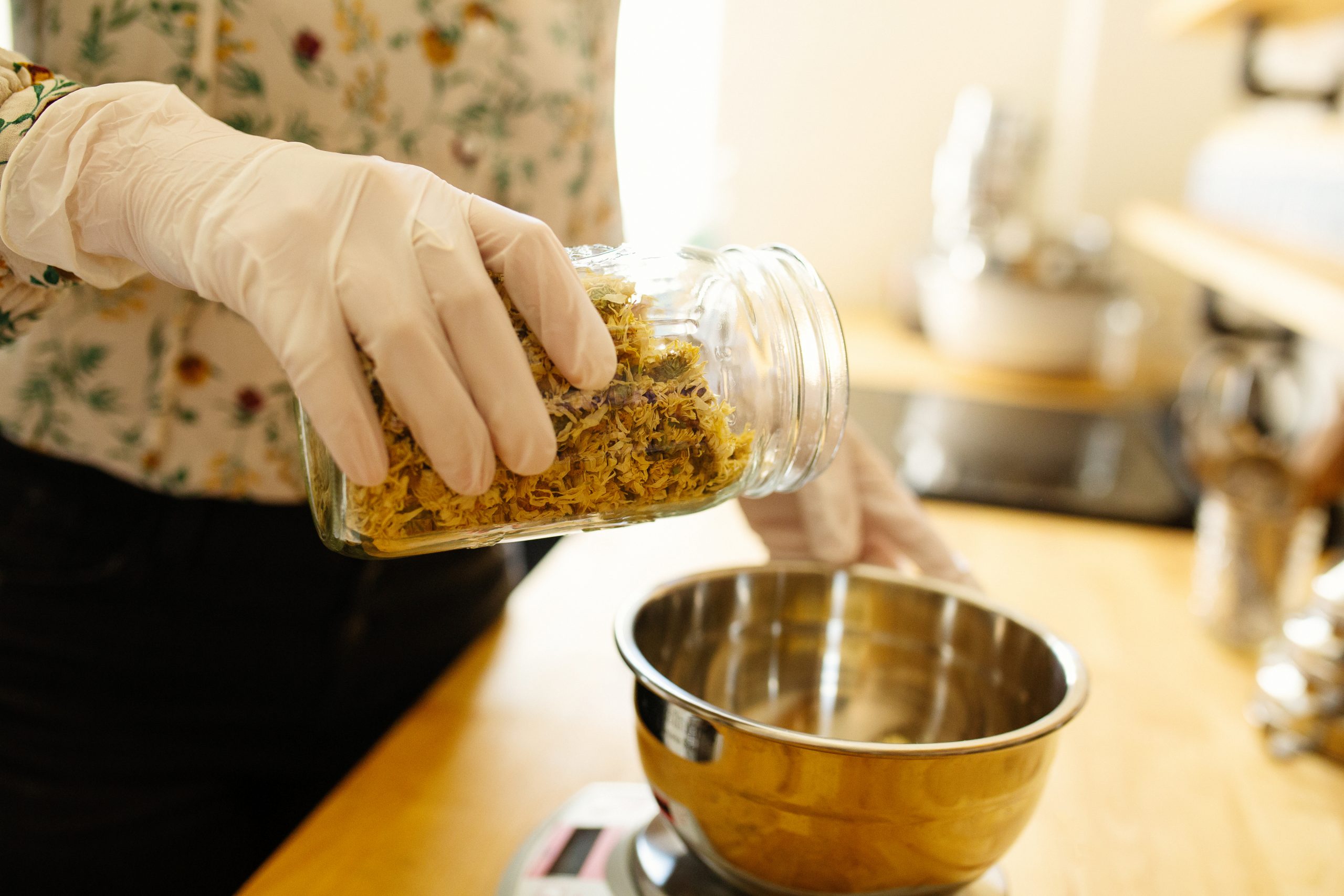 Close up detail shot showing gloved hand, metal bowl and glass jar with herbs. Traditional Chinese herbal medicine. Marketing photography by Ella Sophie, California commercial photographer. 