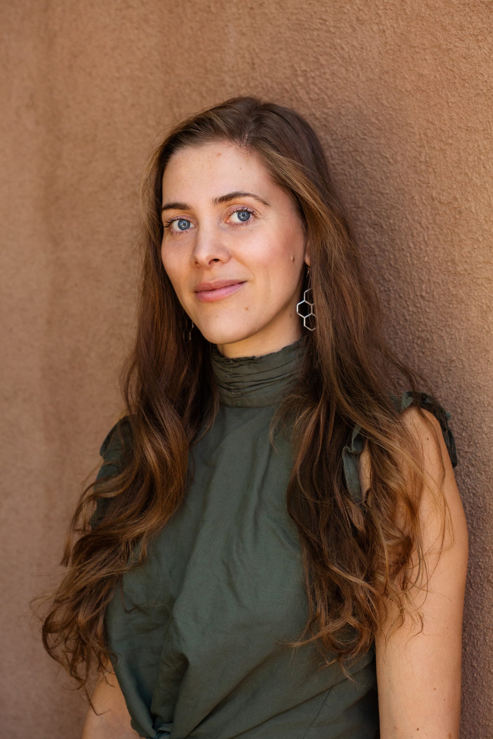 Neutral earth toned portrait photography by Oakland photographer Ella Sophie. Portrait of Dr. Clara Wetmore in Taos NM wearing green shirt in front of brown adobe style wall. 