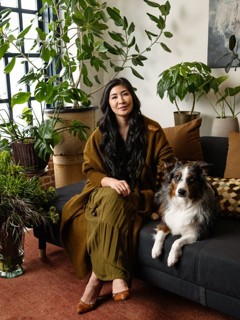 Personal branding portrait of Annie Wu with her service dog, sitting in a plant filled Oakland studio.